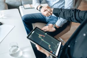 Two businessmen shaking hands as one holds an electronic pad