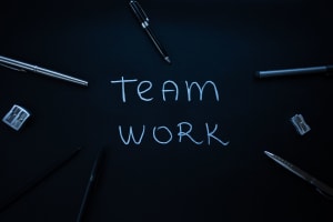 The words 'Team Work" written on a digital blackboard with writing implements and other office supplies around it