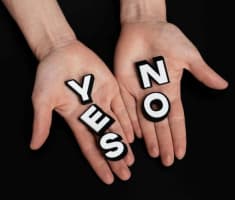 Image of two human hands, one holding the word yes, the other the word no