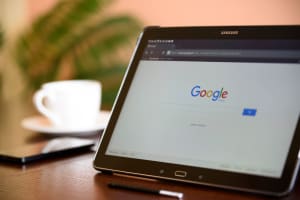 Photo of digital tablet sitting on surface with a Google webpage on screen and a coffee cup beside it