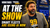 A promotional thumbnail for a Work Truck “Truck Chat” interview filmed at a fleet industry trade show. Large text reads “AT THE SHOW” and “SMART FLEETS ARE USING AI NOW.” A man in a blazer stands in front of an RTA fleet management software booth, speaking about AI and fleet operations.
