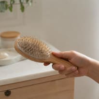 A hand holding a hairbrush, and there is hair in the brush.