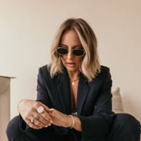 A woman with a short blonde haircut, wearing a suit, sitting, and wearing sunglasses.