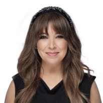 A woman with long brown hair, a black sleeveless blouse, and a beaded headband.