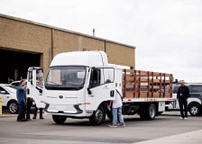 A lot of several vehicles, with the central vehicle being a medium-duty work truck with several workers inspecting it.