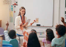 A female teacher sitting in front of elementary school classroom, giving a lesson to several students.