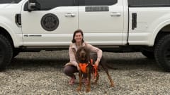 Woman kneeling with a Bloodhound in front of a white pickup truck.