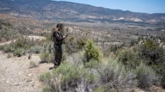 Man standing in desert talking on radio.