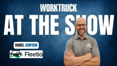 Man standing with arms crossed in front of blue background with Work Truck logo and At The Show in large white letters, plus a Fleetio logo.