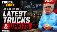 Man standing and talking with clasped hands in front of a poster for Isuzu truck with logo for Truck Chat and Work Truck and headline Latest Trucks & Upfits.