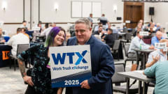 Lauren Fletcher and Wayne Parham pose with a Work Truck Exchange 2025 sign during a networking session while fleet professionals meet in the background.