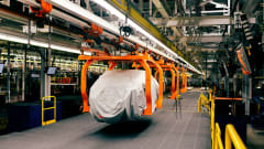 Covered vehicle body suspended from orange overhead production equipment inside Ford’s Louisville Assembly Plant.
