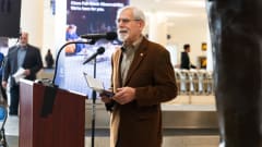 Rod Diridon Sr. speaking at a podium wearing a brown blazer.
