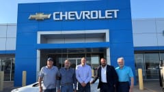 Photo of four men involved in sale of three auto dealerships, standing in front of the sold Chevrolet store
