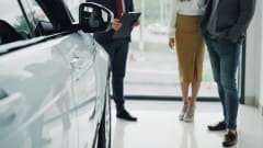 Couple talking with auto salesman next to new car inside dealership