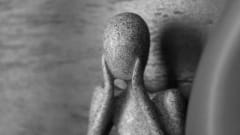 Marble statue holding hands to face.