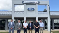 Six men standing in front of a Ford dealership.