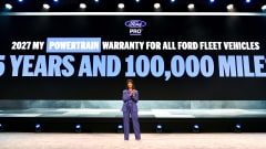 Presenter stands onstage before a large screen announcing Ford Pro’s expanded 5-year, 100,000-mile powertrain warranty for additional fleet vehicles beginning with the 2027 model year.
