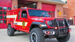 Red Morgan Olson Kestrel fire response truck parked outside a fire station, featuring off-road tires, emergency lights, and equipment compartments for first responder use.