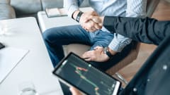 Two businessmen shaking hands as one holds an electronic pad