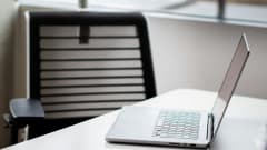 Laptop computer open on desk with empty chair behind it