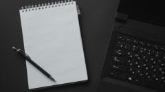 Photo of notepad and pen next to computer keyboard on desk