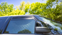 Close-up of the 2027 Volkswagen ID. Buzz side window with quilted privacy shades and integrated side mirror camera parked outdoors.
