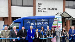 Officials and community leaders cut a ribbon in front of a Pace On Demand shuttle bus outside Rolling Meadows City Hall to celebrate expanded on-demand transit service in northwest Cook County.