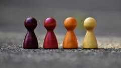 Wooden people figures of different colors in a row, similar to board game pieces
