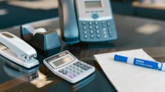 Photo of an land-line phone on a desk with various office supplies