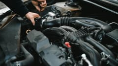 Photo of man working under the hood of a car with a tool