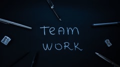 The words 'Team Work" written on a digital blackboard with writing implements and other office supplies around it