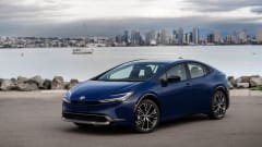 Photo of blue Toyota Prius parked next to body of water with city skyline in background