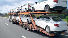 A double-decker stinger car hauler carries a full load of new white vehicles along an interstate highway.