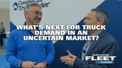 Two men discuss commercial truck market trends at an industry event, with text about uncertain truck demand and Automotive Fleet branding in the background.