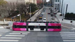 An pink and white OKC streetcar moves down a street. 