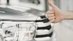 car in background with hand giving a thumbs up in front
