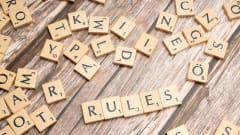 Scrabble tiles  spelling out 'Rules' among random letter tiles, all on a wooden surface