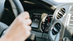 Photo of a woman's hand gripping a steering wheel with the dashboard display in the background