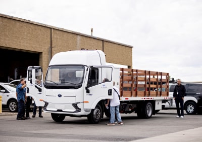 A lot of several vehicles, with the central vehicle being a medium-duty work truck with several workers inspecting it.