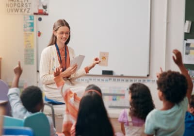 A female teacher sitting in front of elementary school classroom, giving a lesson to several students.