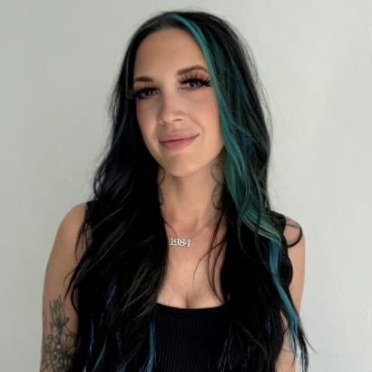 A young woman with long black and green hair, in a black crop top. 