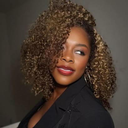 A woman in black, with tight, carmel curls,  looks over her shoulder.