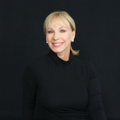 A blonde woman with a ponytail, wearing a black turtleneck and jeans, sitting.