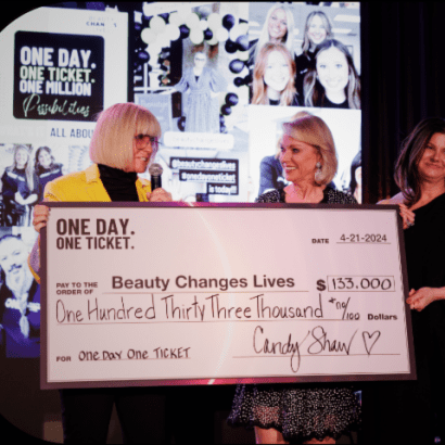 Two happy women, one wearing yellow blazer, are smiling and holding an oversized check.