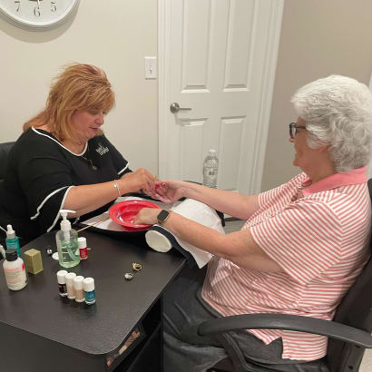 Two women face each other over a manicure table, as one woman gives the other woman a manicure.
