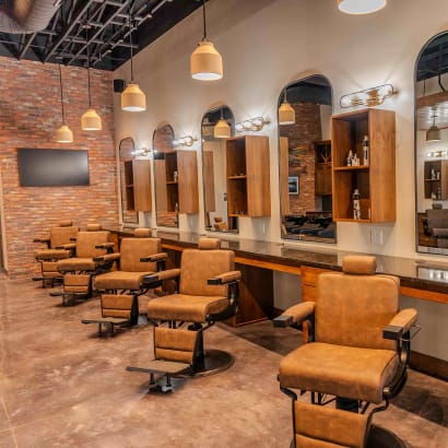 A row of brown barbershop chairs, stations and large arched mirrors at Parlor by Thompson and Company.