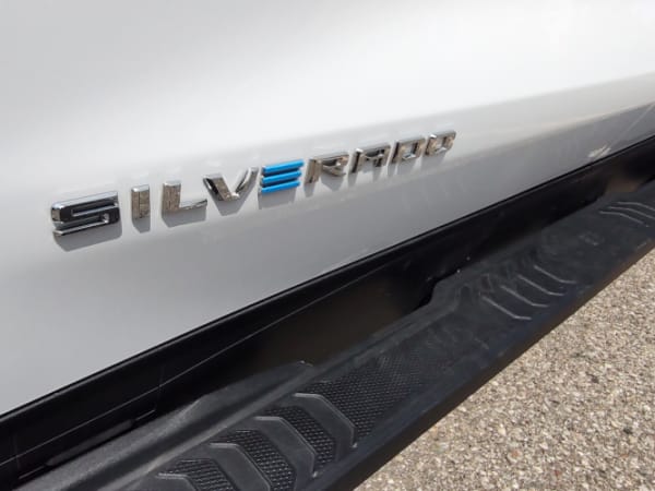 Close up photo of the side of a white truck with the word Silverado in chrome, the E is in blue to signify it as an electric vehicle.