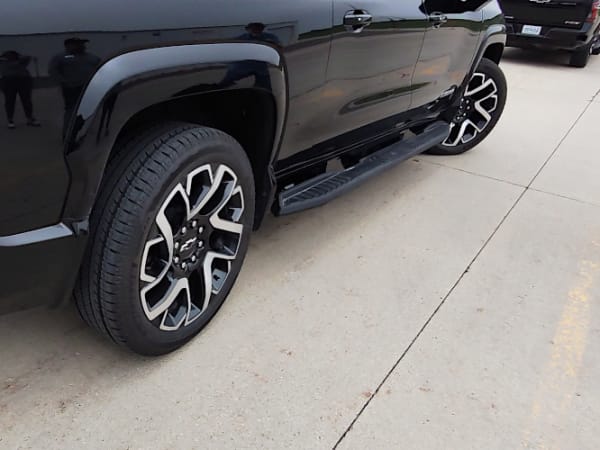 Close-up view of a black pickup truck with front wheels turned to the right and rear wheels turned in the opposite direction to demonstrate all-wheel-steering.