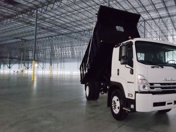 An Isuzu truck with a dump bed inside a building, with the bed tipped up.